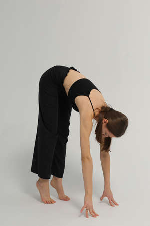 Slim young woman wearing flared black trousers and black top, tall, long hands, tip-toeing, bending...