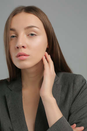 Portrait of pretty young woman of natural beauty, without makeup, full lips, long straight brown hair with parting, looking at camera, wearing classic jacket, isolated on grey backgroundの写真素材