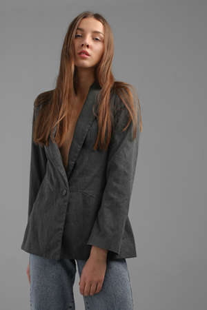 Fashionable portrait of young woman without make up, natural beauty, with chestnut long hair, wearing oversized grey jacket on naked body, in studio, grey backgroundの写真素材