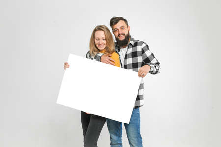 young loving couple, bearded man and blondie are smiling, hugging, holding blank banner, isolated on white background, Advertisement concept. Mockup for designの写真素材