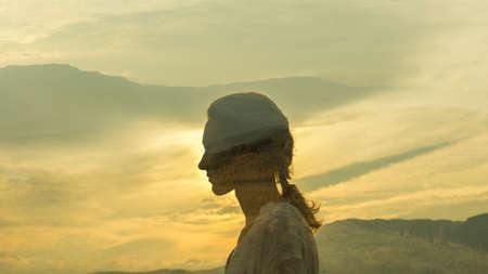 warm profile double exposure portrait of young woman with plaited hair during duskの写真素材