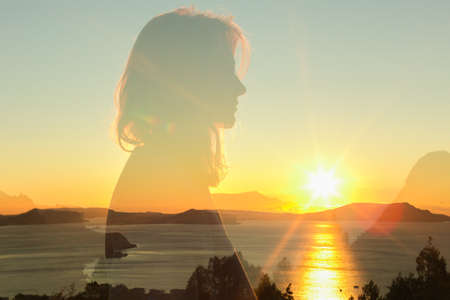double exposure warm profile portrait of young woman wearing sweatshirt, sea , hills and sunrise on...
