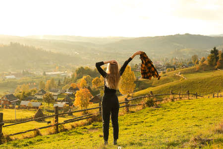 Young woman with scarf on meadow at sunset in autumn, back view