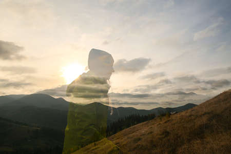 Silhouette of a man standing on the top of the mountain and looking at the sunsetの写真素材