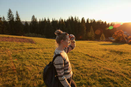 Young woman with backpack taking photos on mountain meadow at sunset. Space for textの写真素材
