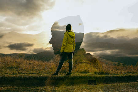 Person in yellow jacket standing on the edge of a cliff and looking at the mountain landscapeの写真素材