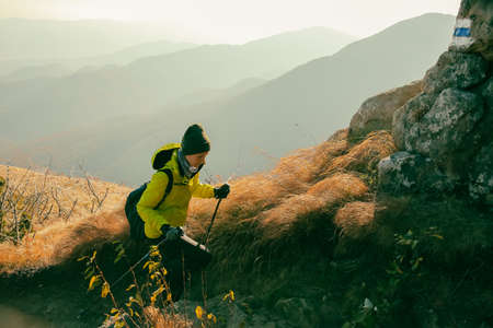A man in a yellow jacket and a black cap sits on the edge of a mountain and looks into the distance.の写真素材