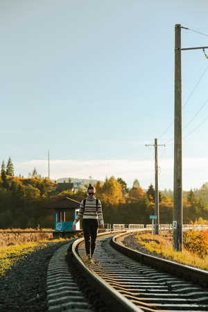 A woman with a backpack walks along the railway tracks in the autumn.の写真素材