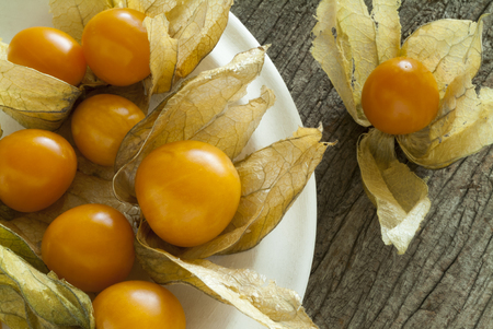 Close up of Golden Berries with husks in a white plate on a rustic wood surface.の写真素材