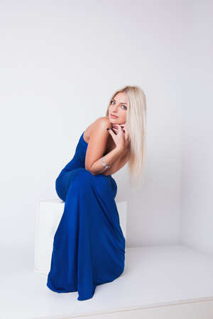 Portrait of pretty sexy young woman with long blonde hair in blue dress sittingの写真素材