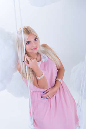 Portrait of a sexy young woman in pink dress swinging in the clouds. Studio photoの写真素材