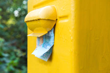 Money sticking out of a yellow mailbox