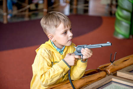 Little boy shooting with revolver gun in amusement park. He is playing