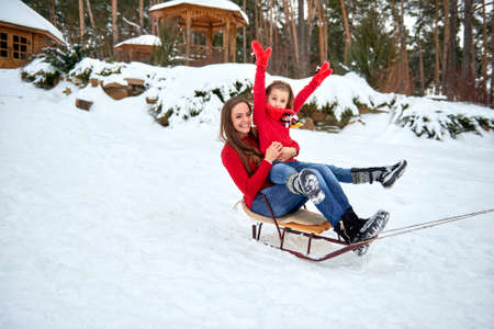 Mother and daughter sledding and laughing on the snow in forest.の写真素材