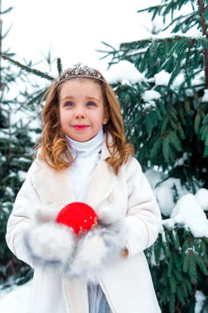 Little girl near green fir trees on the snowの写真素材