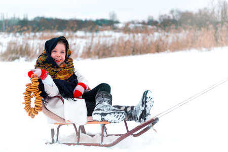 little girl in a fur coat with bagels on sledge