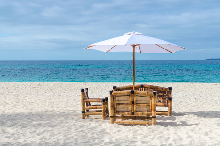 Tropical beach resort view with turquoise sea, lonely beach table with chairs from bamboo and umbrella on exotic white sandy Puka beach on Boracay, Philippinesの写真素材