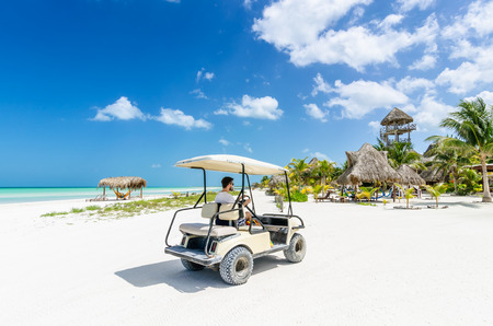 Cute young man driving golf cart along tropical white sandy beach during his Caribbean vacation on...