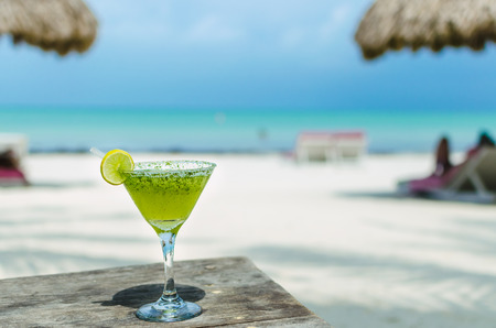 Fresh cold tasty Margarita cocktail with lime and ice on a table at tropical white sand beachの写真素材