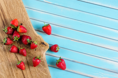 Ripe juicy sweet strawberries on wooden domestic cutting board over styled old aged wooden turquoise table. Vintage background with free copy text space.の写真素材
