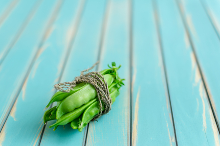A bunch of fresh pods of green peas roped with a twine on stylized old aged wooden turquoise board background close-up, with selective focus. Rustic background with free text space.の写真素材