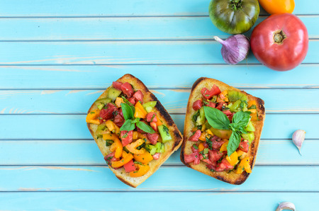 Fresh homemade rustic style bruschetta with red, yellow and green tomatoes, fresh basil, garlic and...