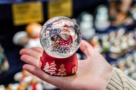 Beautiful christmas red snowdome with Santa Claus inside on palm close-up at Christmas market in kioskの写真素材