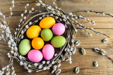 Easter background with copy space. Homemade hand painted colorful easter eggs in nest from willow branches over retro wooden rustic background, top viewの写真素材