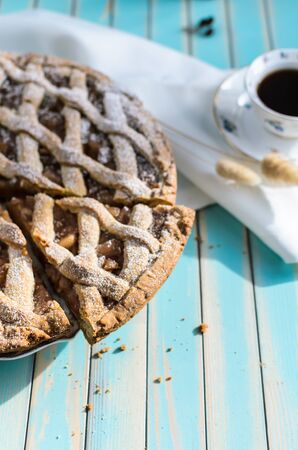Baked homemade rustic apple tart pie with cutted piece with crumbs in ceramic dish next to a cup of coffee and white napkin over wooden turquoise table background with natural side sunlight, selective focusの写真素材