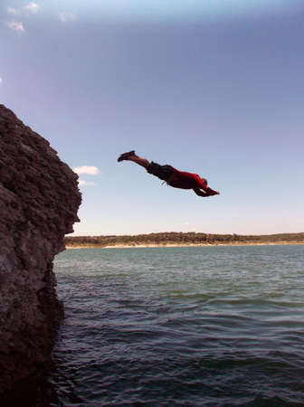 Heavyset man dives off cliff into a lakeの写真素材