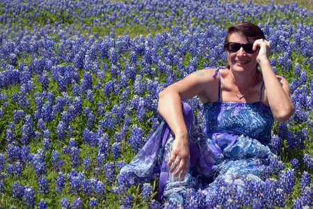 A women in blue dress smiling in a field of Texas Bluebonnets, holding her sunglasses.の写真素材