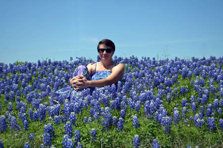A women in a dress sitting in a field of Texas Bluebonnets.の写真素材
