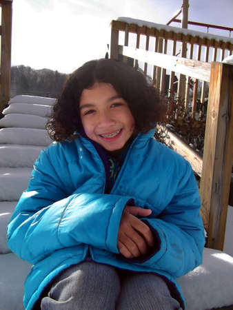 Young child in puffy blue coat, smiling and showing off her new dental bracesの写真素材