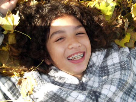 Close up of Smiling child with braces laying in Leavesの写真素材