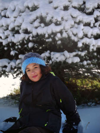 Girl with curly brown hair sitting in front of snowy treeの写真素材