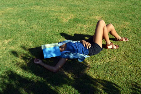 Tan teenage girl laying on the grass with a book over her faceの写真素材