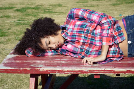 Mixed race teen girl sleeping on picnic tableの写真素材