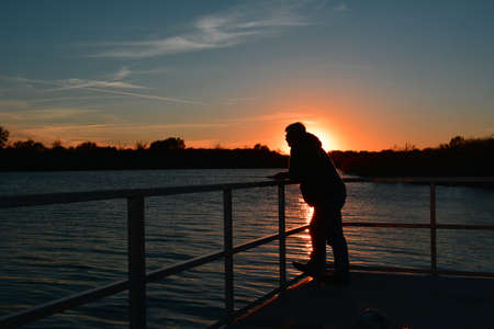 Man fishing from a dock backed by a reflecting sunsetの写真素材