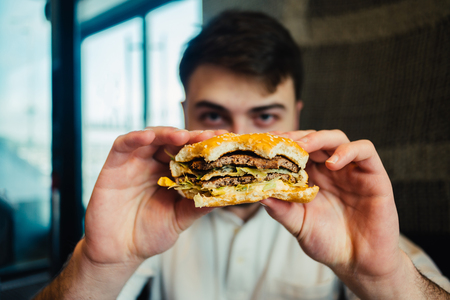 young man holding a tasty and hamburhen going to eat it. Focus is shown in full face food outletsの写真素材