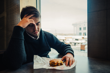 Portrait of a young bearded man in black sitting in the restaurant and fast food can no longer eatの写真素材