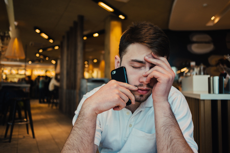 frustrated young businessman with a beard talking on the phone in the cozy restaurantの写真素材
