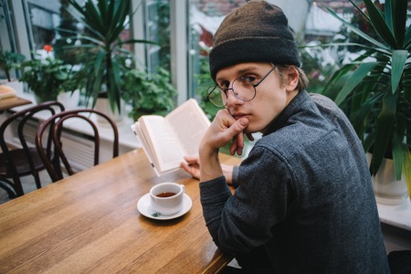 young student sitting and drinking tea and reading interesting book in the beautiful cafe during a break at the universityの写真素材