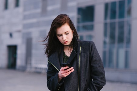 young beautiful brunette business woman uses a mobile phone on a background of cityscapeの写真素材