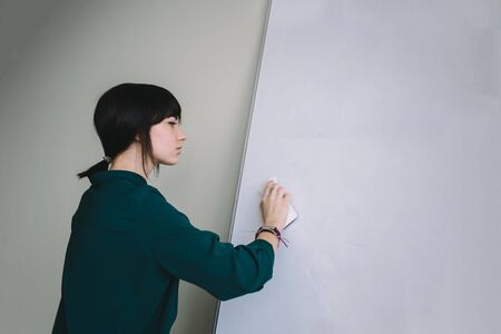 The young woman wipes inscriptions with white board marker...の写真素材