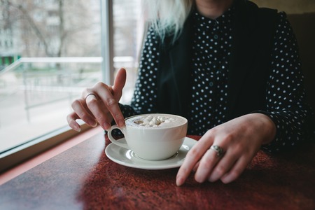 Hands girls take a cup of coffee with marshmallows in a cozy cafe. Hot drink for breakfast. Breakfast in the cafe.の写真素材