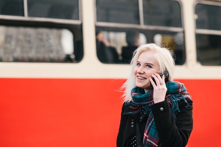 young blonde smiling girl talking on the phone on a background of red train.の写真素材