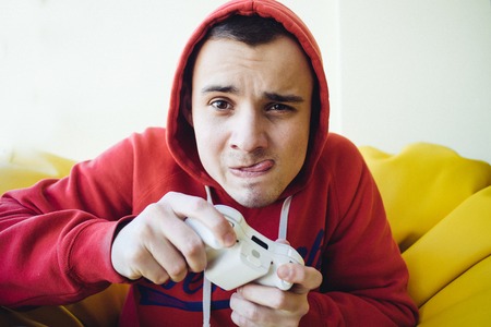 Funny emotional young gamer plays a joystick on the console. Focused view of the camera.の写真素材