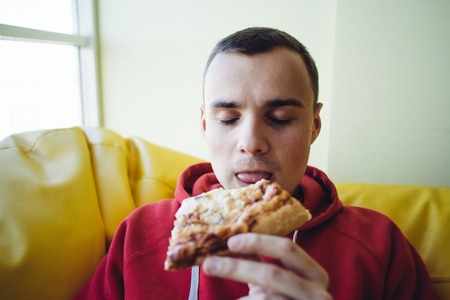 Man eating pizza. Cheerful young man eating pizza at the restaurant. Beautiful young man enjoying a delicious slice of hot pizza. Fastfood during a break at workの写真素材