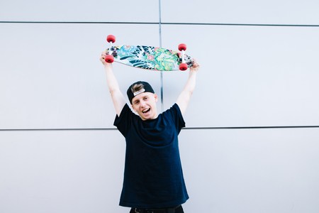 Happy young teenager skater raised the board over his head and rejoices. Joyful skater on a gray background.の写真素材
