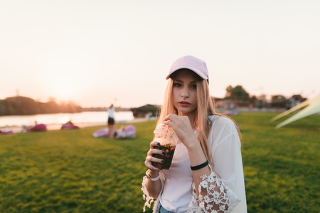 Portrait of a bridal young woman standing against the background of the sun with lemonade in his hands. Walk around the park.の写真素材